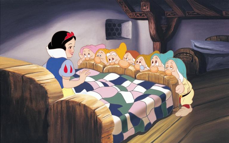 Branca de Neve sentada na cama com os sete anões a olhando da cabeceira
