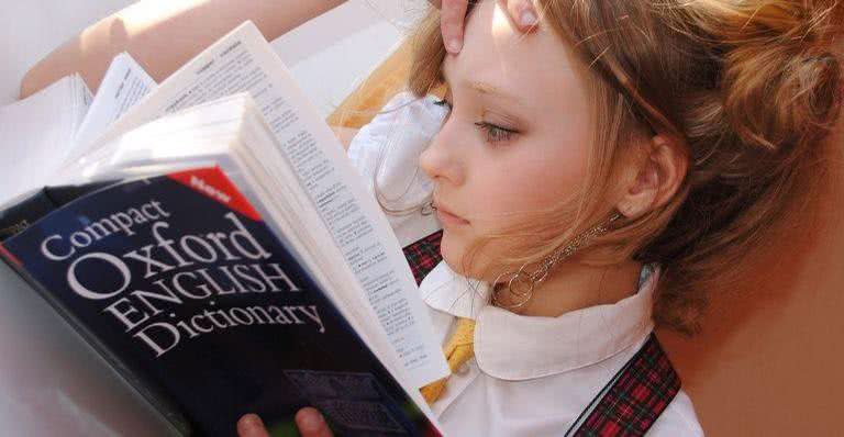 Imagem ilustrativa de uma menina com um dicionário na mão - Pixabay