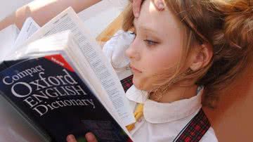 Imagem ilustrativa de uma menina com um dicionário na mão - Pixabay