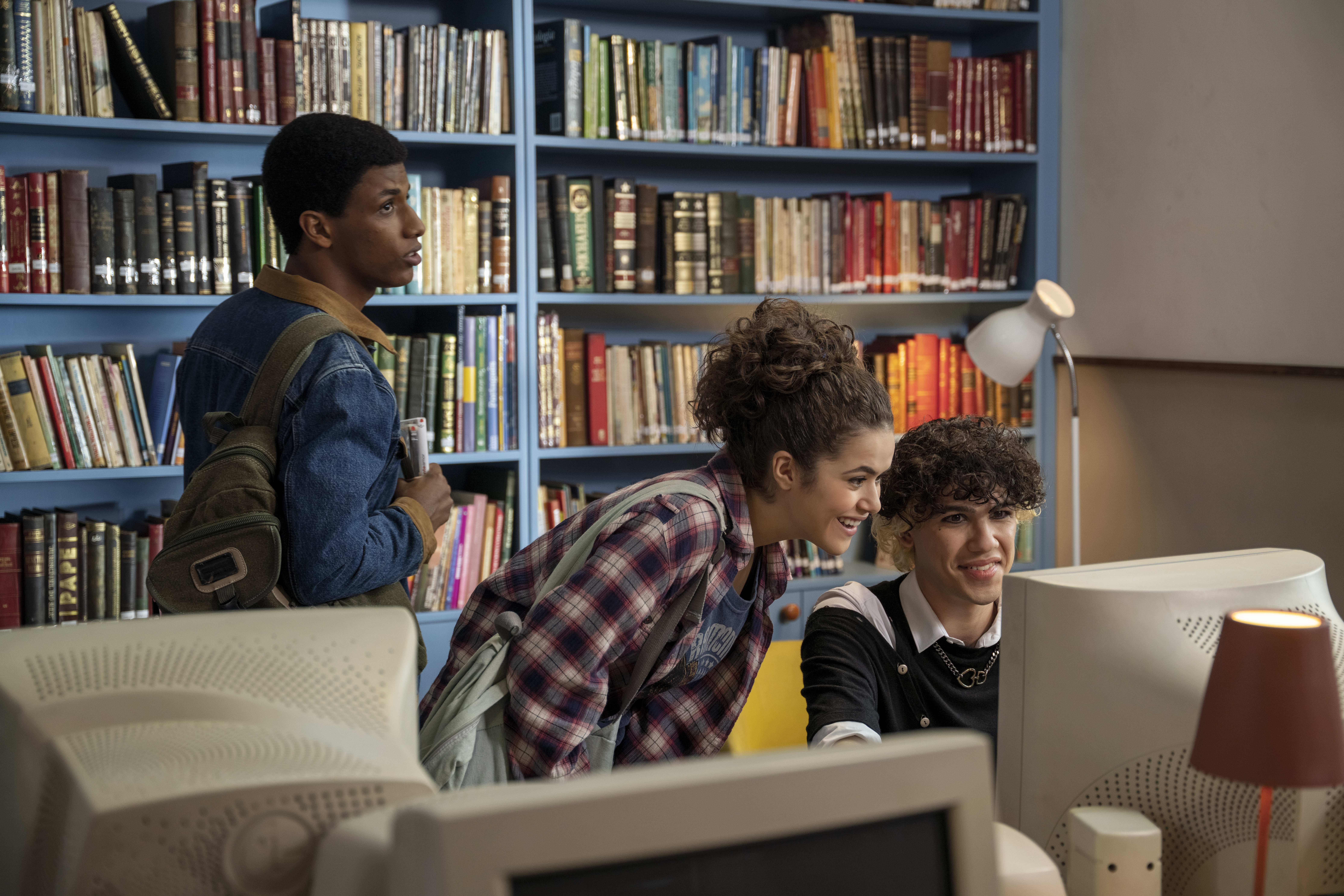 Três jovens em uma biblioteca olhando para a tela de um computador branco